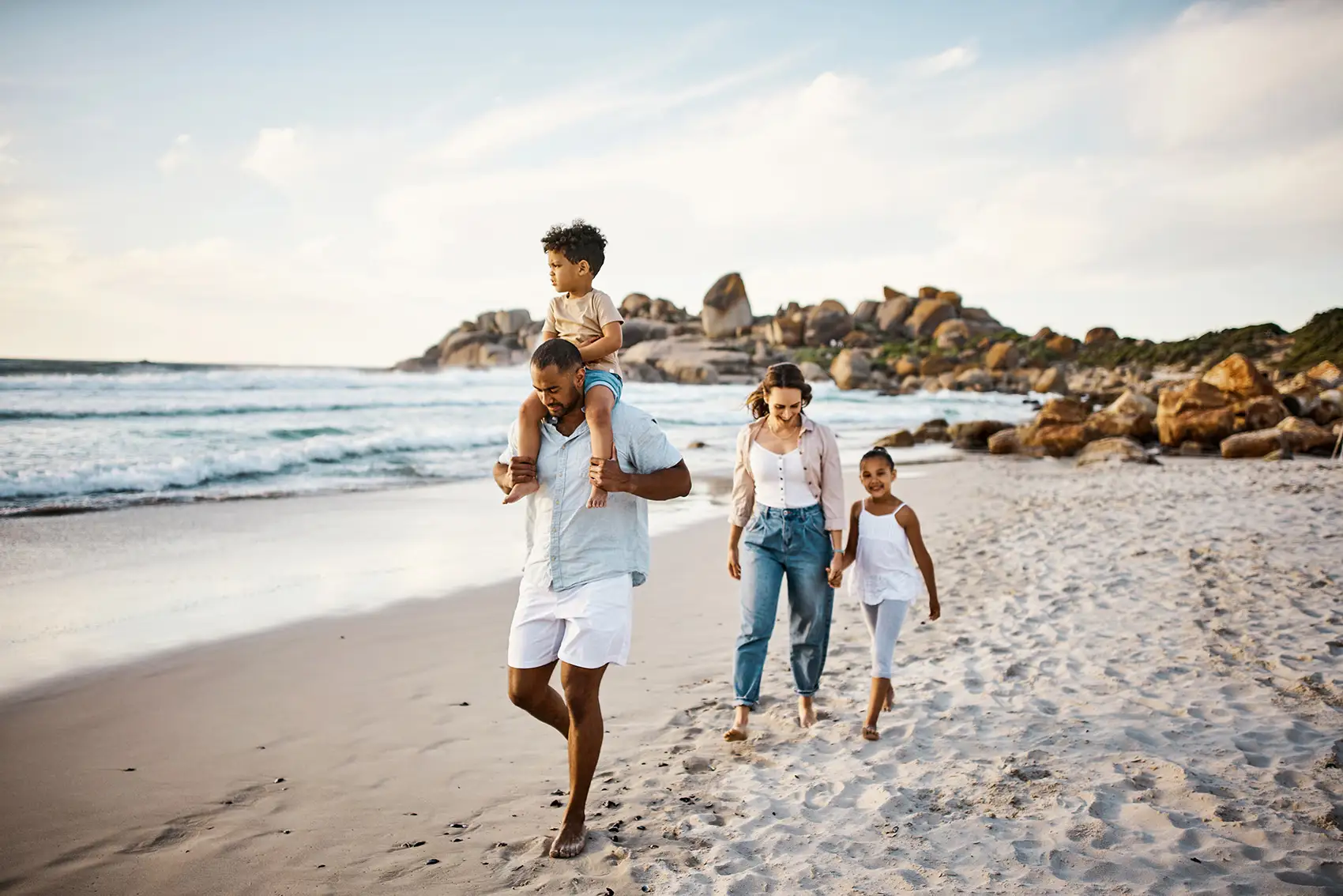 Family walking along a rocky beach, a child on his father’s shoulders