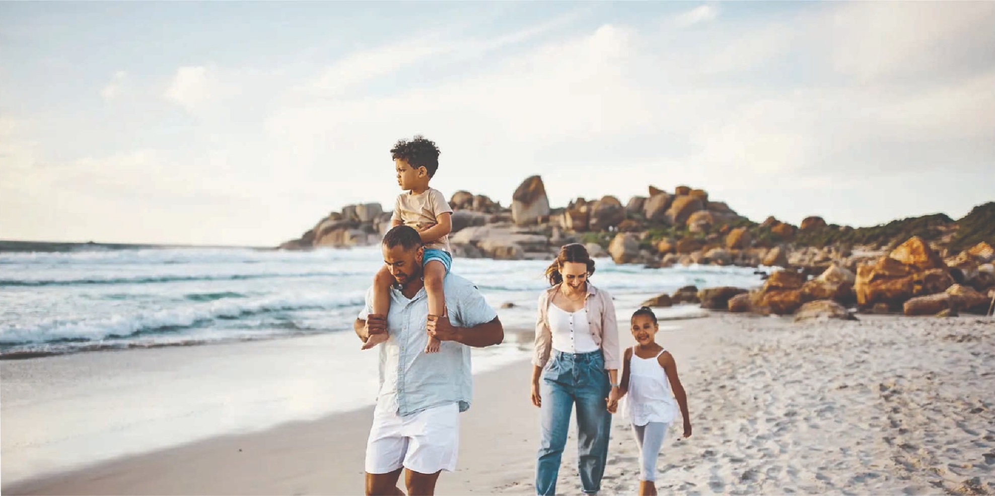 Family walking along a rocky beach, a child on his father’s shoulders