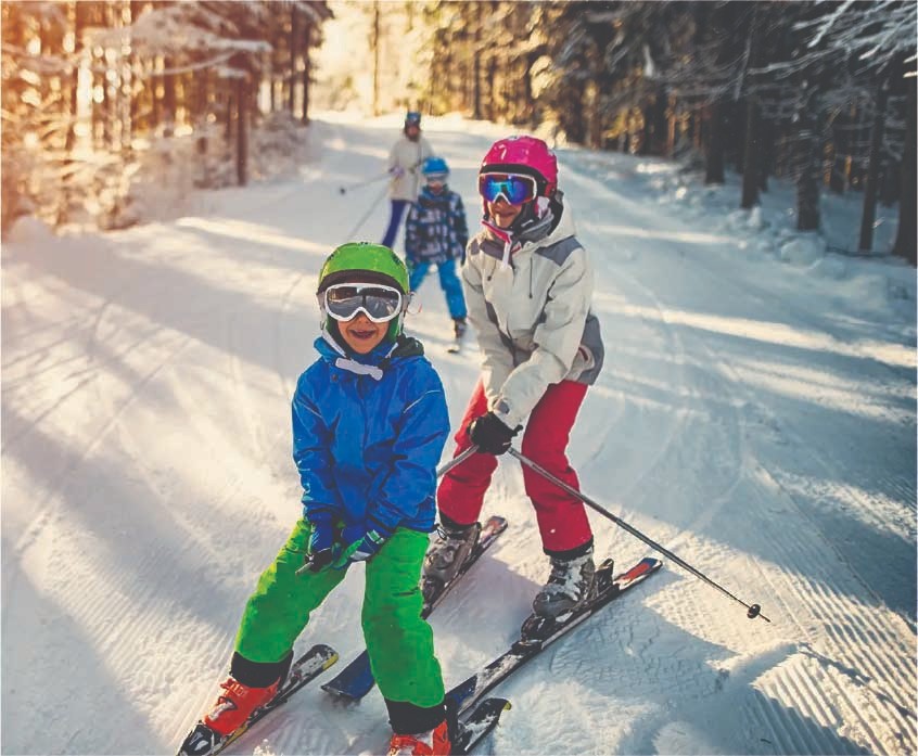 Two children skiing down a snowy forest trail with a parent