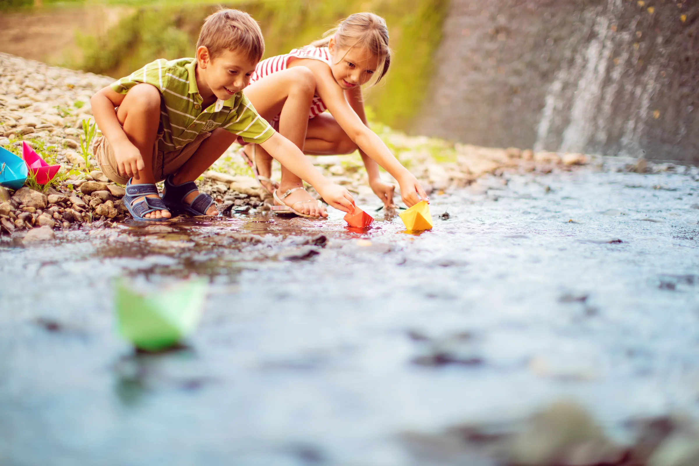 Children floating paper boats in a creek