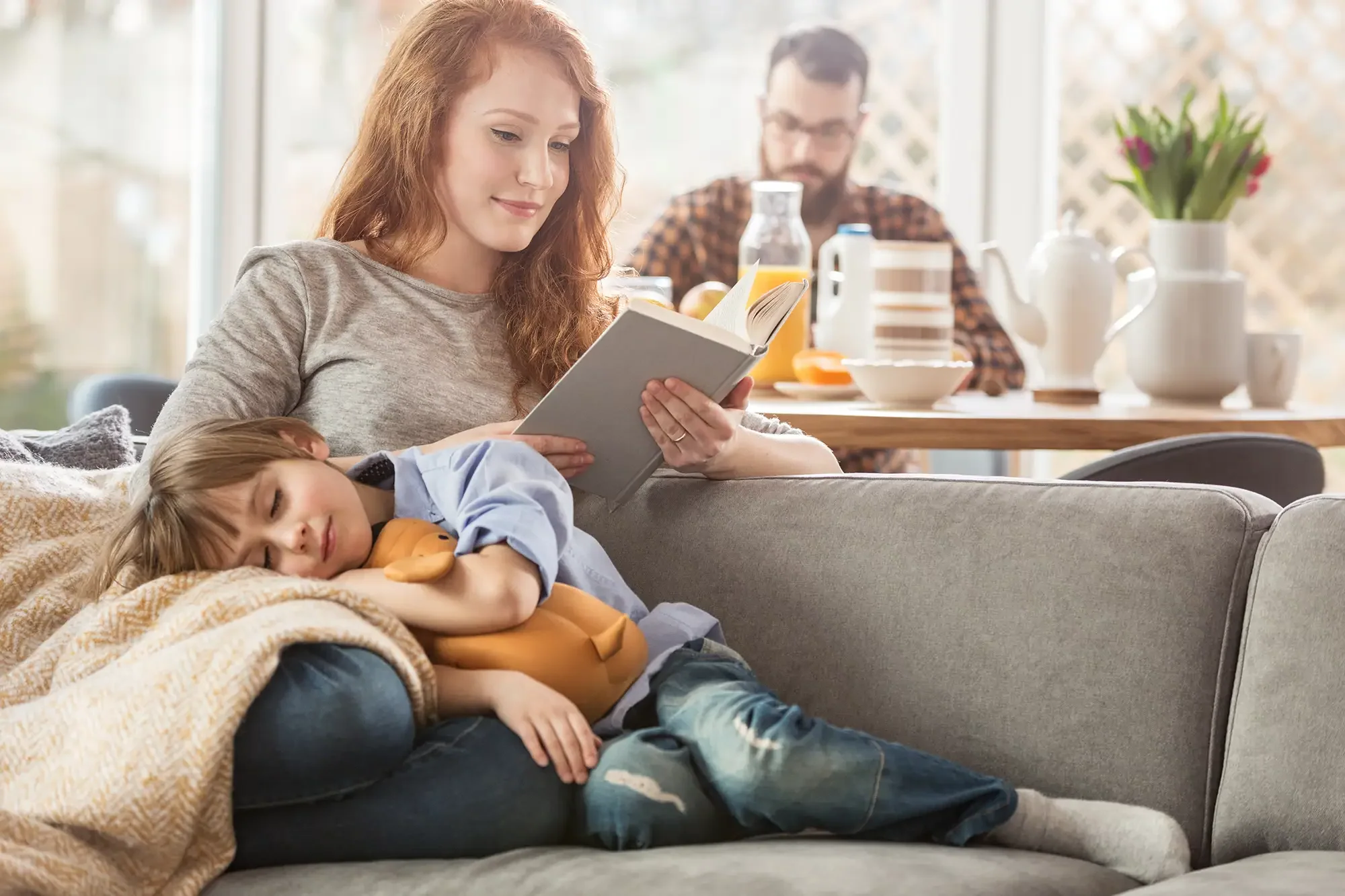 Mother reading on the sofa while her child naps