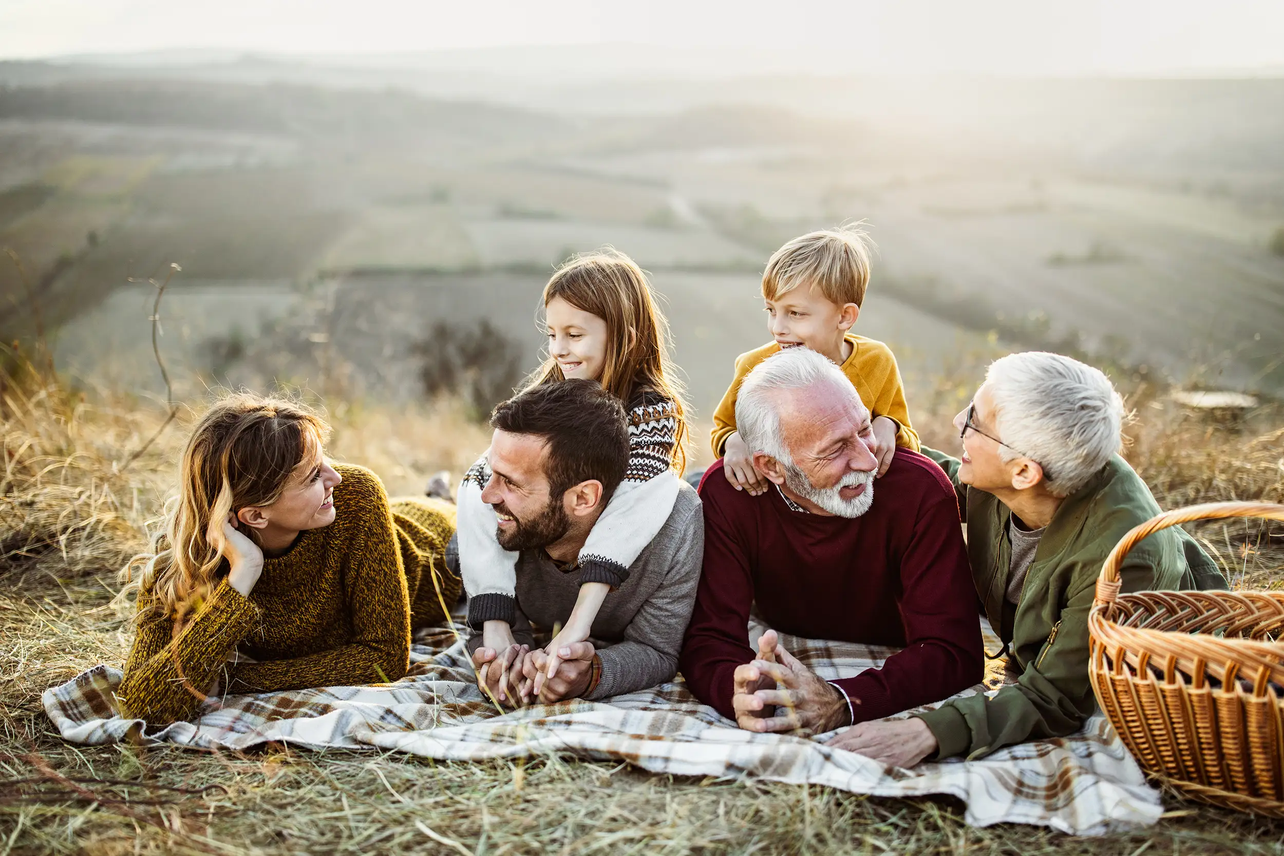 Grandparents, parents and children laughing together on a picnic blanket